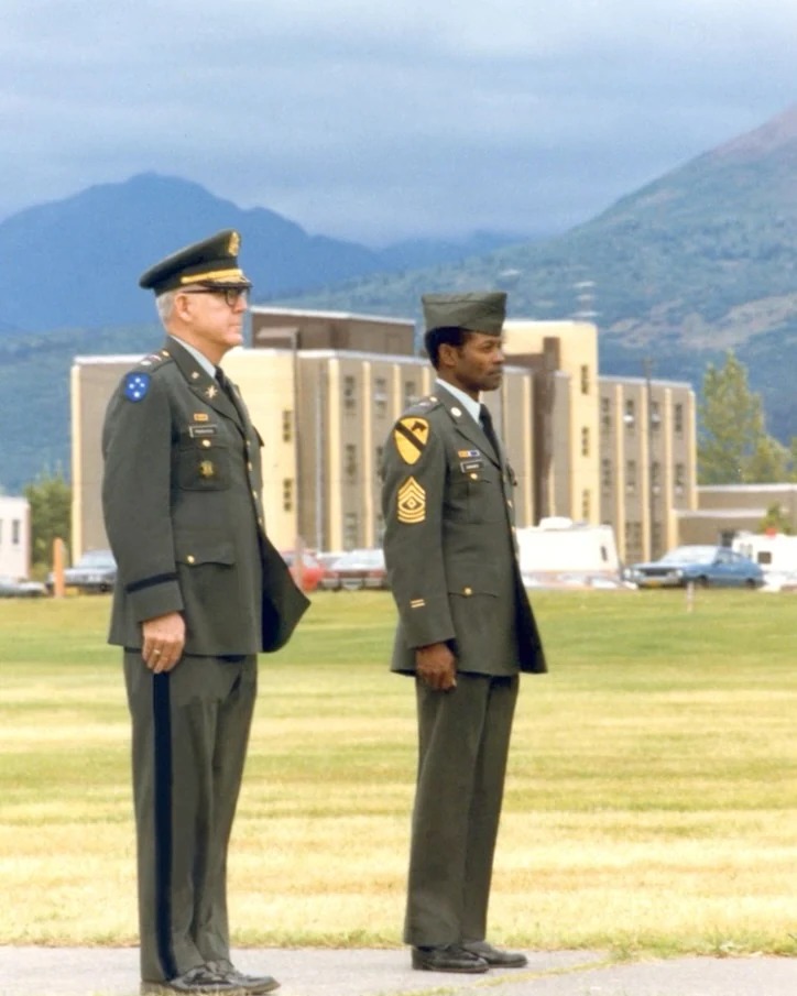 First Sergeant Claude Edwards in U.S. Army dress uniform standing in formation beside a commanding officer in Anchorage, Alaska in the 1980s, Chugach mountains behind them